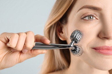 Photo of Young woman using metal face roller on light grey background, closeup