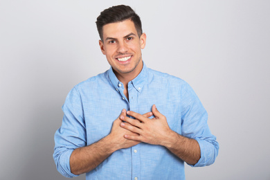 Handsome grateful man with hands on chest against light grey background