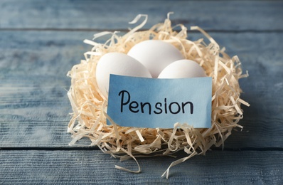 Photo of Eggs and card with word PENSION in nest on wooden background