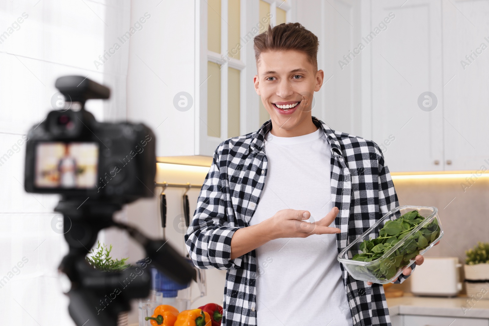 Photo of Smiling food blogger talking about spinach while recording video in kitchen