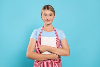 Photo of Beautiful young woman in clean striped apron with tablet on light blue background