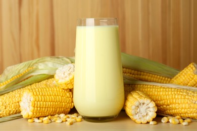 Photo of Tasty fresh corn milk in glass and cobs on wooden table