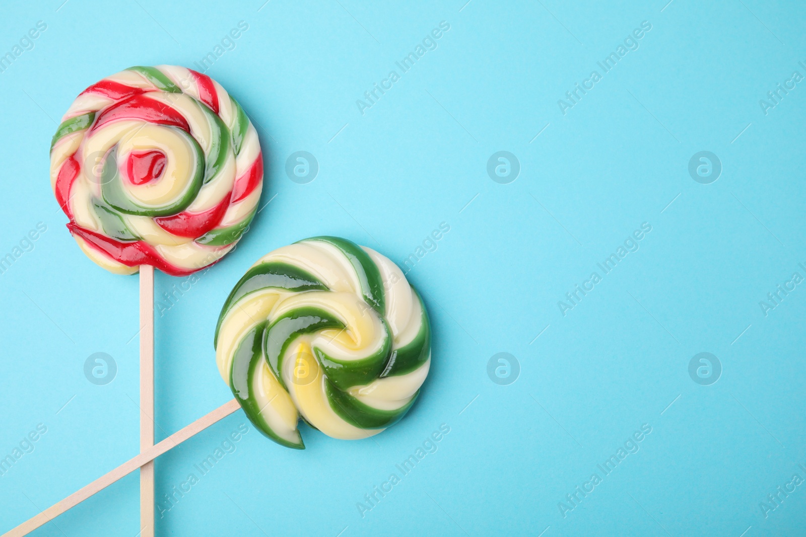 Photo of Colorful lollipops on light blue background, flat lay. Space for text