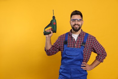 Young worker in uniform with power drill on yellow background. Space for text