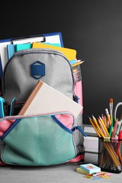 Photo of Backpack with different school stationery on grey wooden table near blackboard