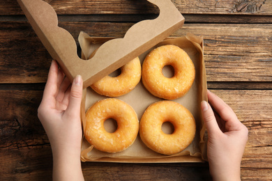 Woman with box of delicious donuts at wooden table, top view