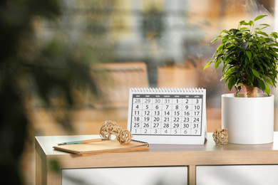 Photo of Paper calendar and plant on wooden table indoors