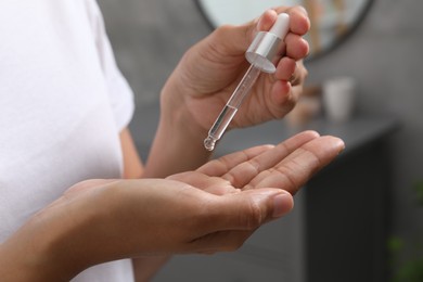 Woman applying cosmetic serum onto her hand indoors, closeup