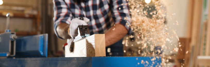 Image of Professional carpenter grinding wooden board with jack plane in workshop, closeup. Banner design