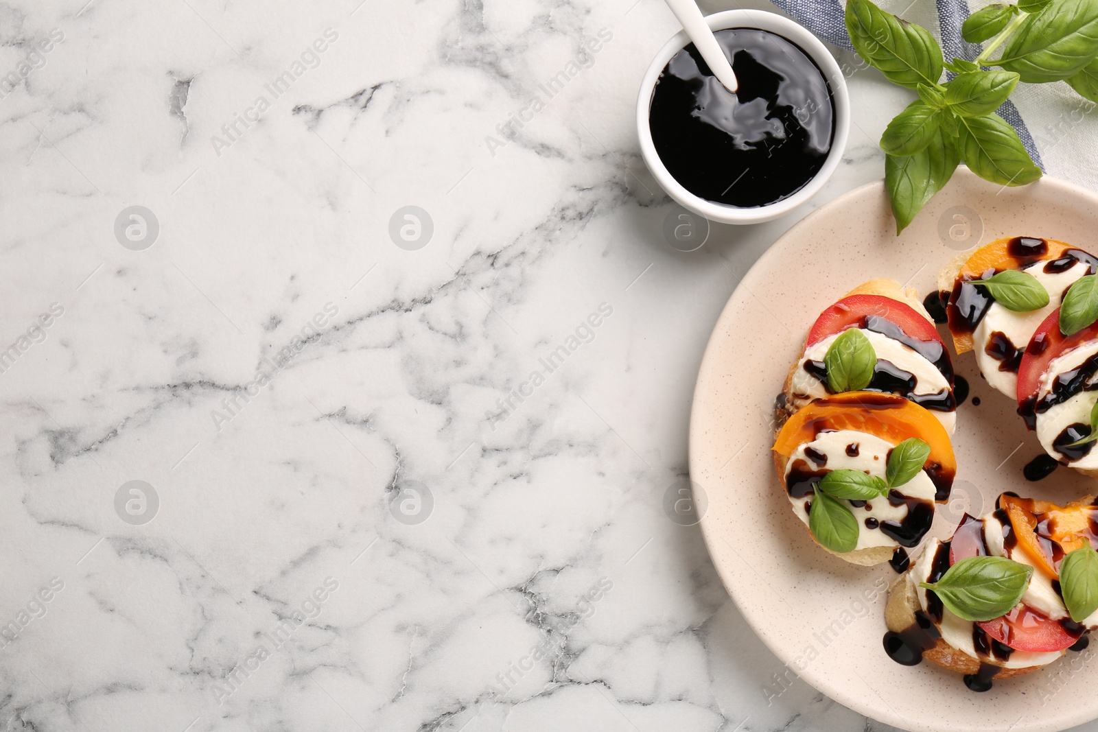 Photo of Delicious bruschettas with mozzarella cheese, tomatoes, balsamic vinegar and ingredients on white marble table, flat lay. Space for text