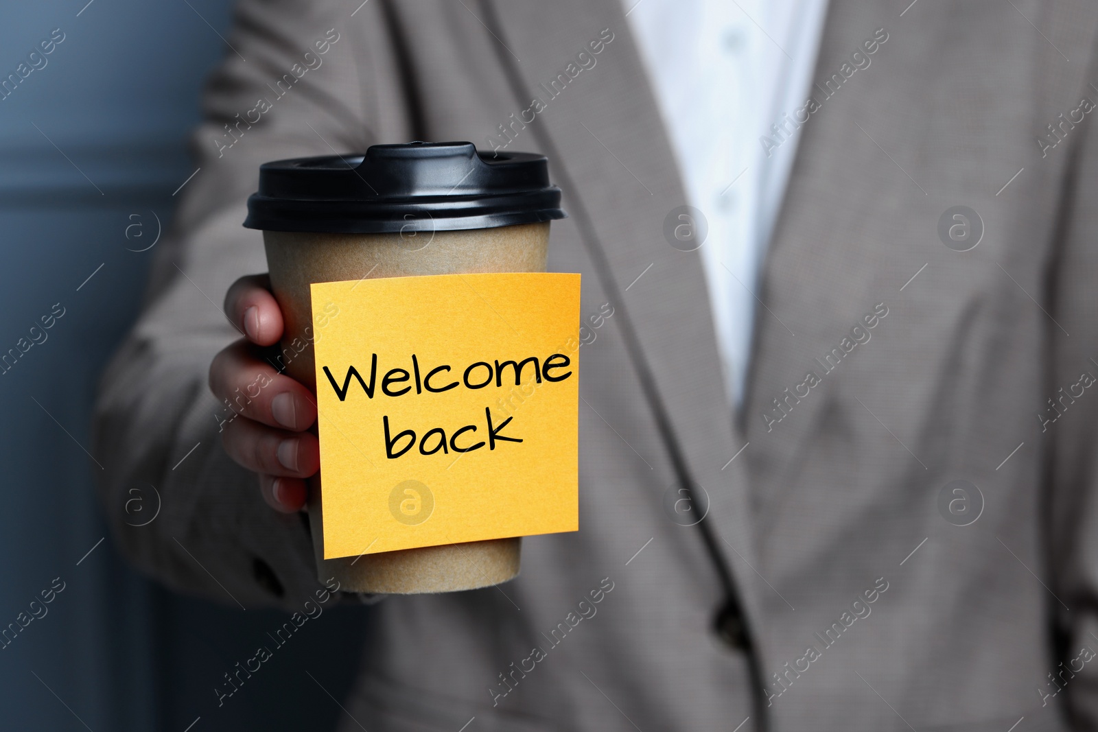 Image of Woman holding paper coffee cup with Welcome Back sticky note, closeup