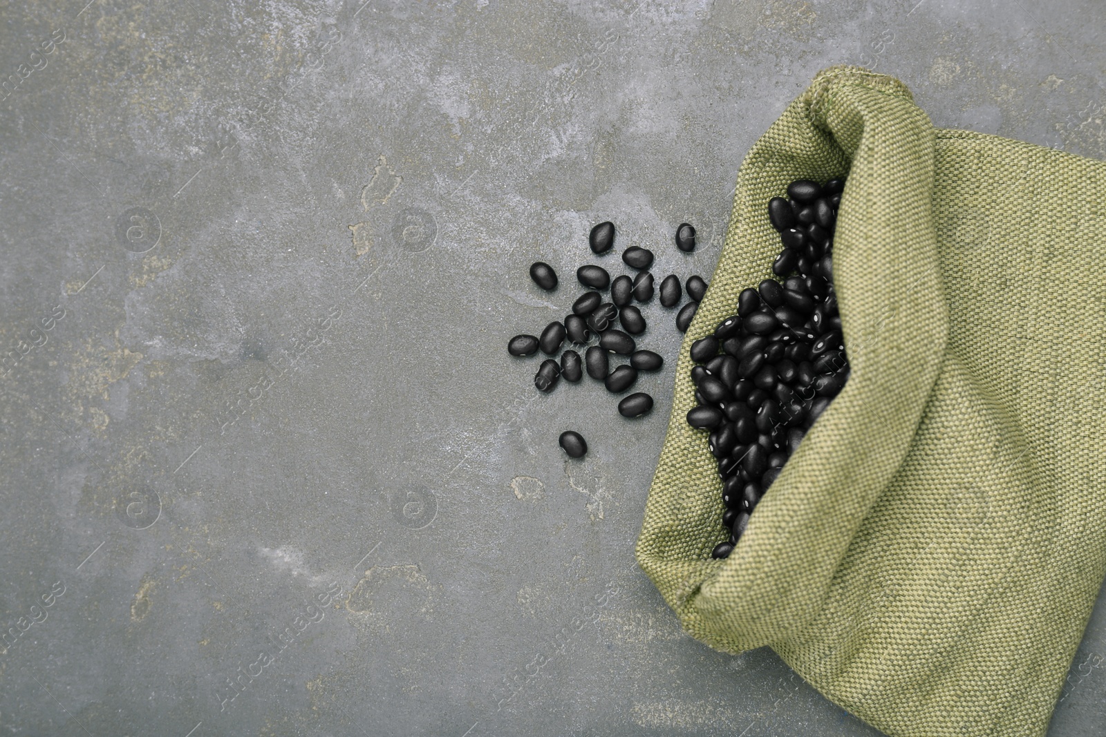 Photo of Sack of raw black beans on grey table, top view. Space for text