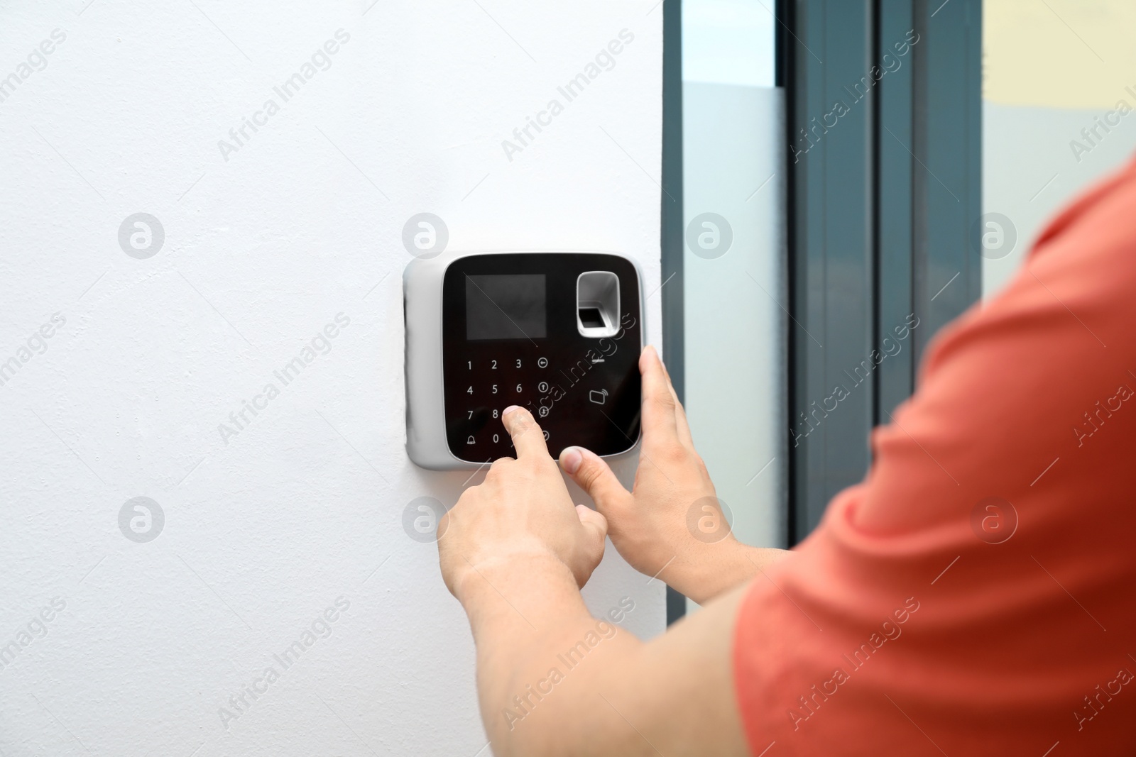 Photo of Young man entering code on alarm system keypad indoors