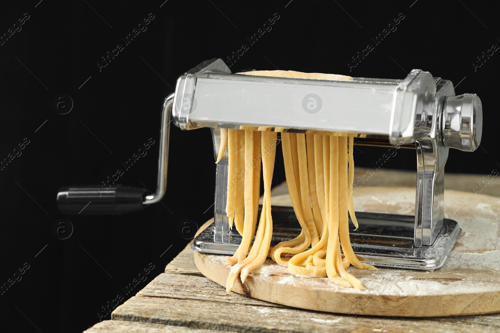 Photo of Pasta maker with raw dough on wooden table against black background, closeup