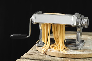 Pasta maker with raw dough on wooden table against black background, closeup