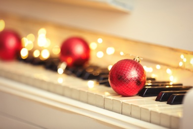 Red bauble and fairy lights on piano keys, space for text. Christmas music