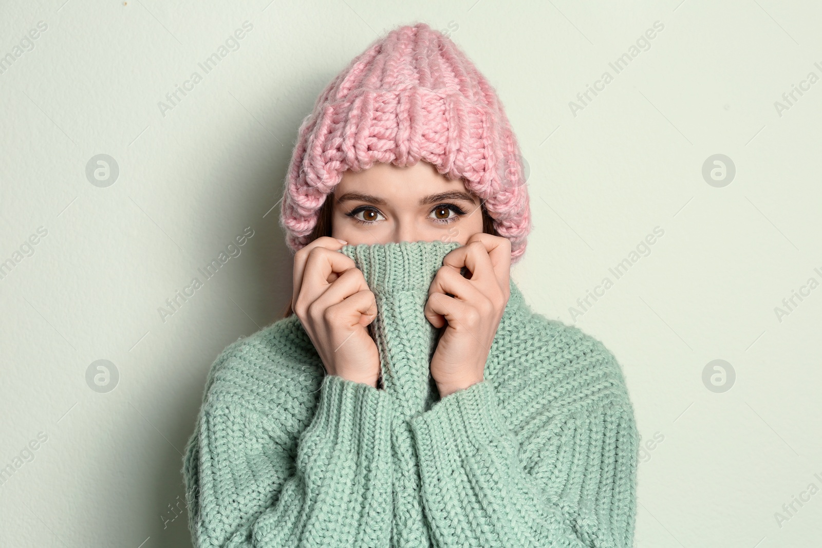 Photo of Young woman wearing warm sweater and hat on light background. Winter season