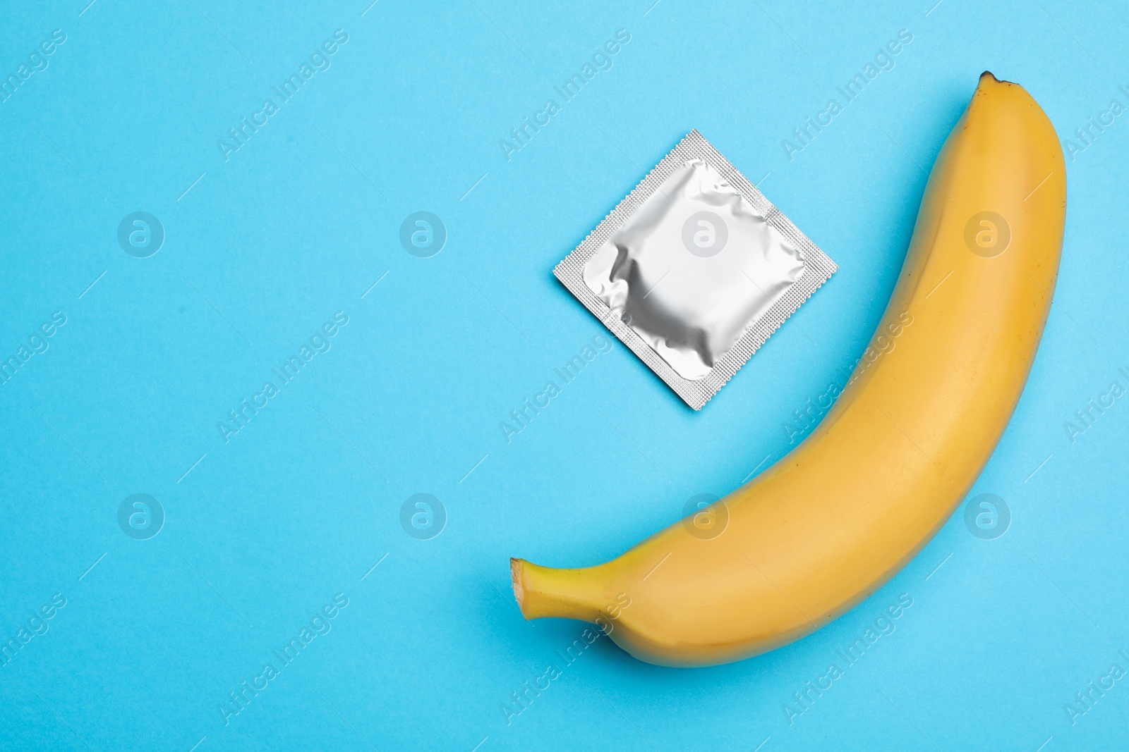 Photo of Condom with banana and space for text on light blue background, flat lay. Safe sex