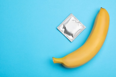 Photo of Condom with banana and space for text on light blue background, flat lay. Safe sex