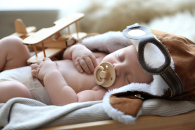 Cute newborn baby wearing aviator hat with toy sleeping in wooden crate