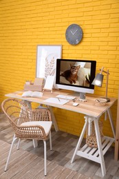 Stylish home office interior with comfortable workplace near yellow brick wall