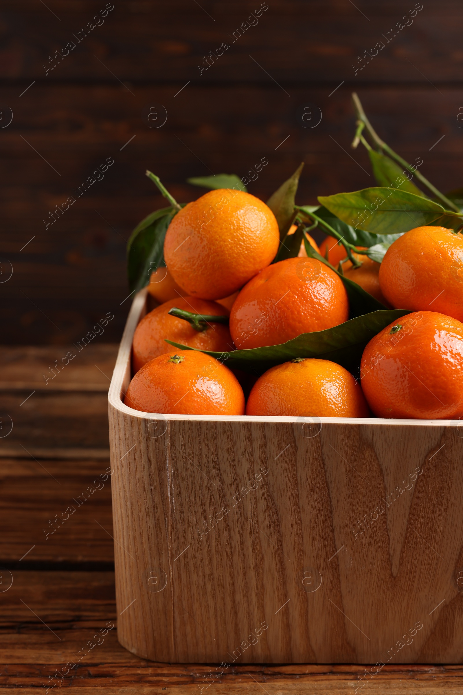 Photo of Fresh tangerines with green leaves in crate on wooden table, closeup