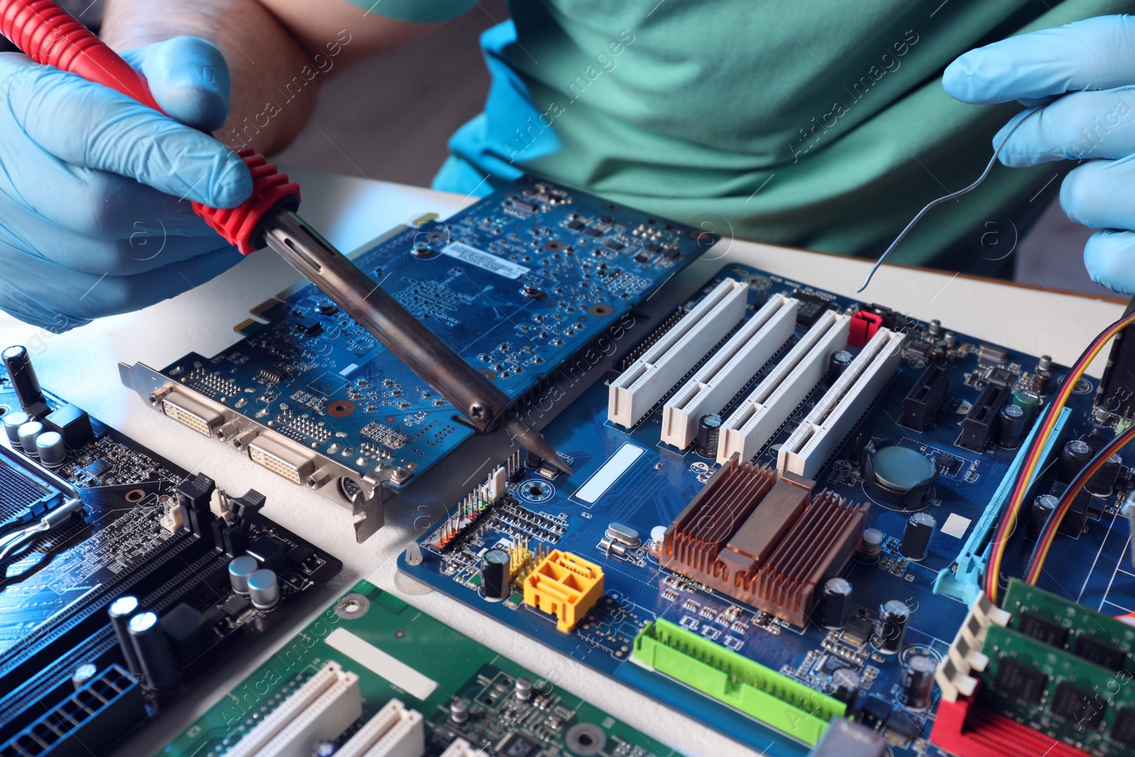 Photo of Technician repairing electronic circuit board with soldering iron at table, closeup