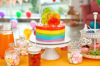 Photo of Bright birthday cake and other treats on table in decorated room