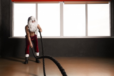 Photo of Young shirtless Santa Claus training with ropes in modern gym