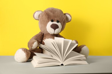 Teddy bear and open book on light table against yellow background