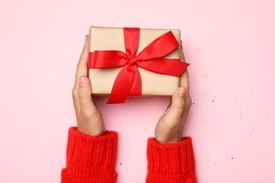 Young woman holding Christmas gift on pink background, top view