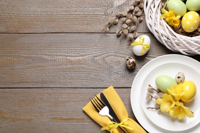 Photo of Festive Easter table setting with painted eggs and flowers on wooden background, flat lay. Space for text