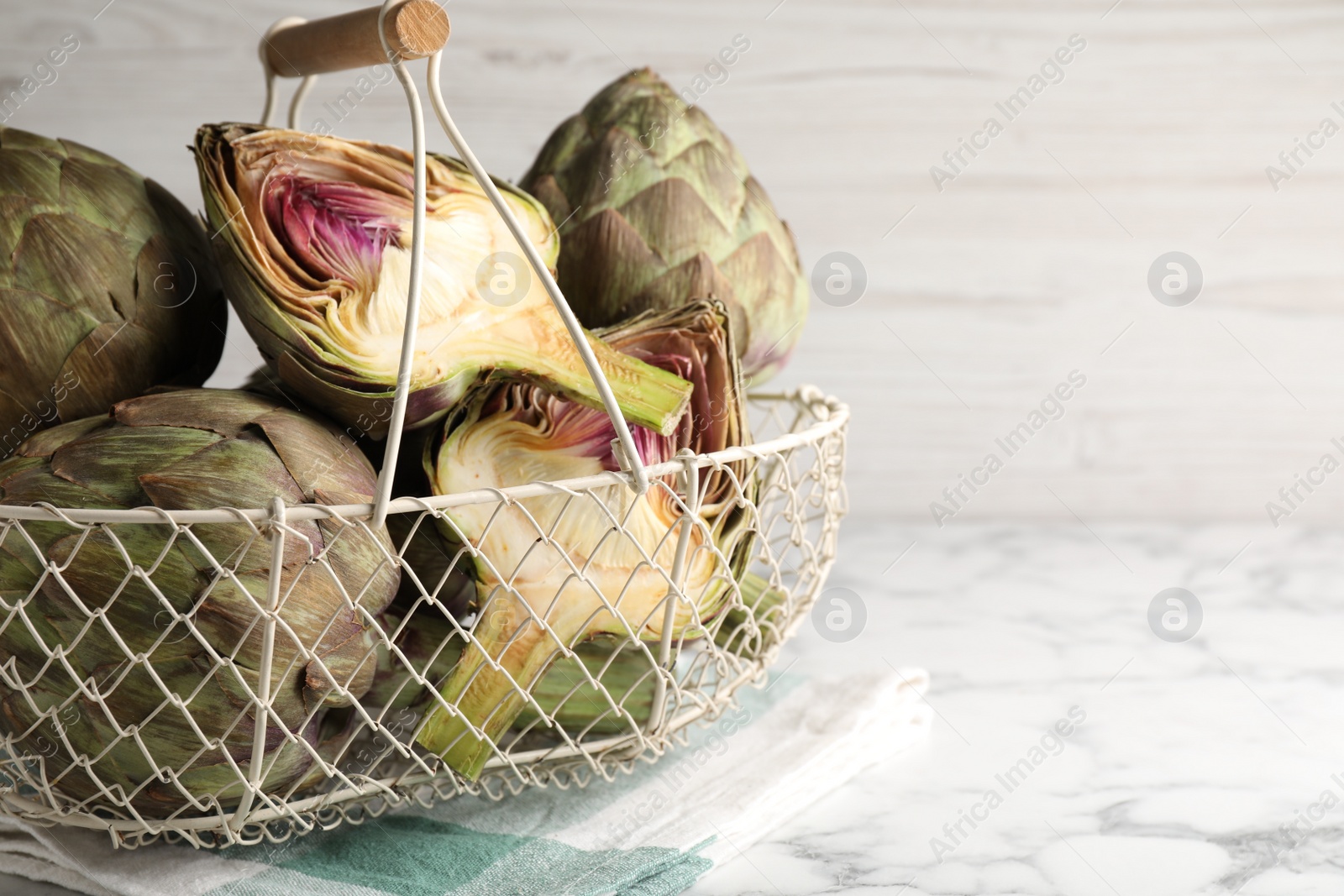Photo of Cut and whole fresh raw artichokes on white marble table, space for text