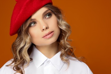 Portrait of beautiful young woman in stylish beret against orange background, closeup