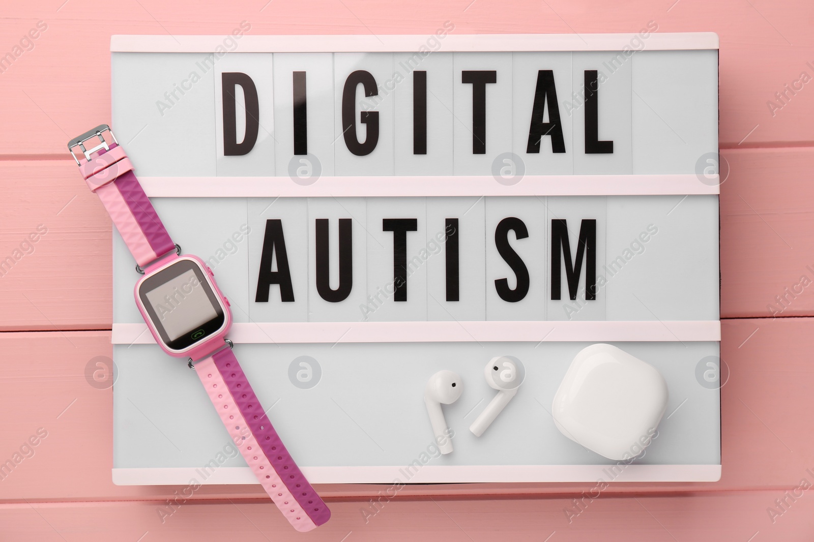 Photo of Lightbox with phrase Digital Autism, smartwatch and earphones on pink wooden table, top view