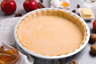 Photo of Raw dough and ingredients for traditional English apple pie on light grey table, closeup