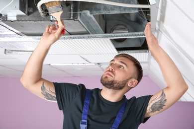 Photo of Young male technician cleaning air conditioner indoors