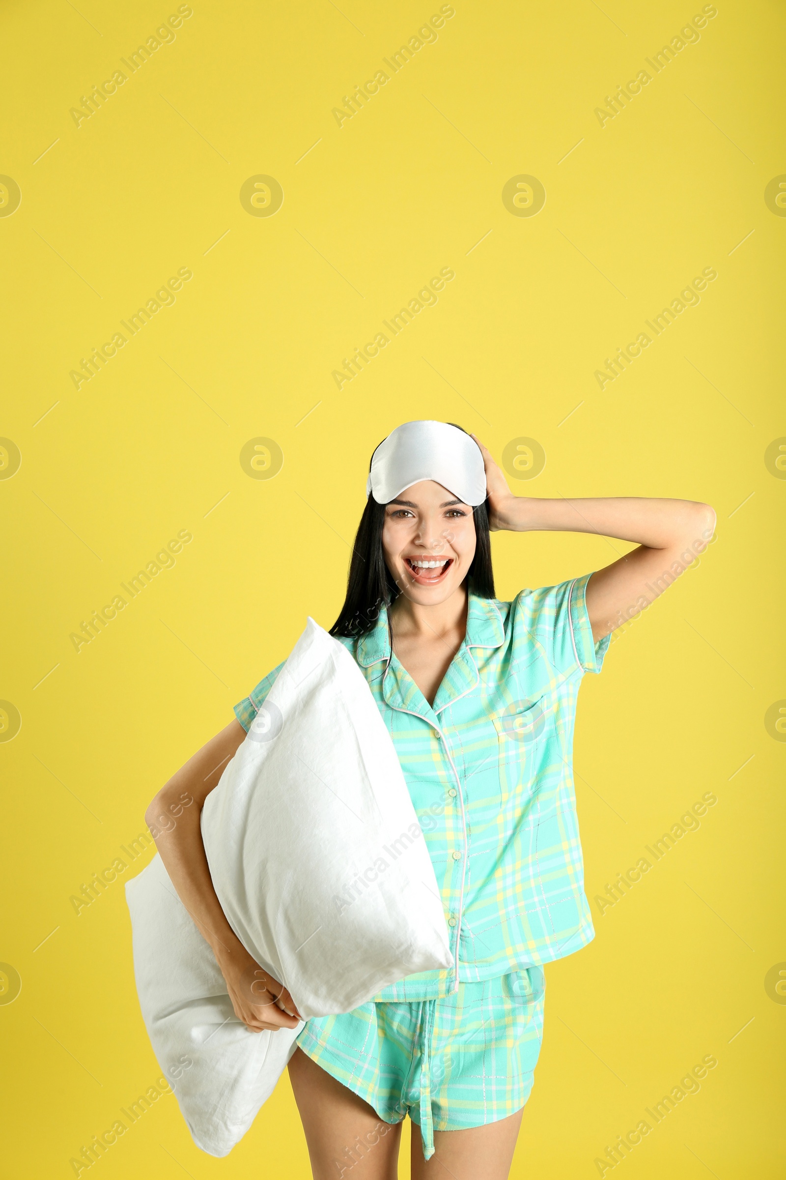 Photo of Young woman with pillow and sleep mask on yellow background