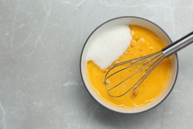 Photo of Bowl with whisked eggs and sugar on light grey table, top view. Space for text