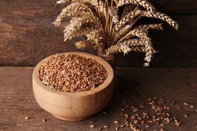 Photo of Wheat grains in bowl and spikes on wooden table