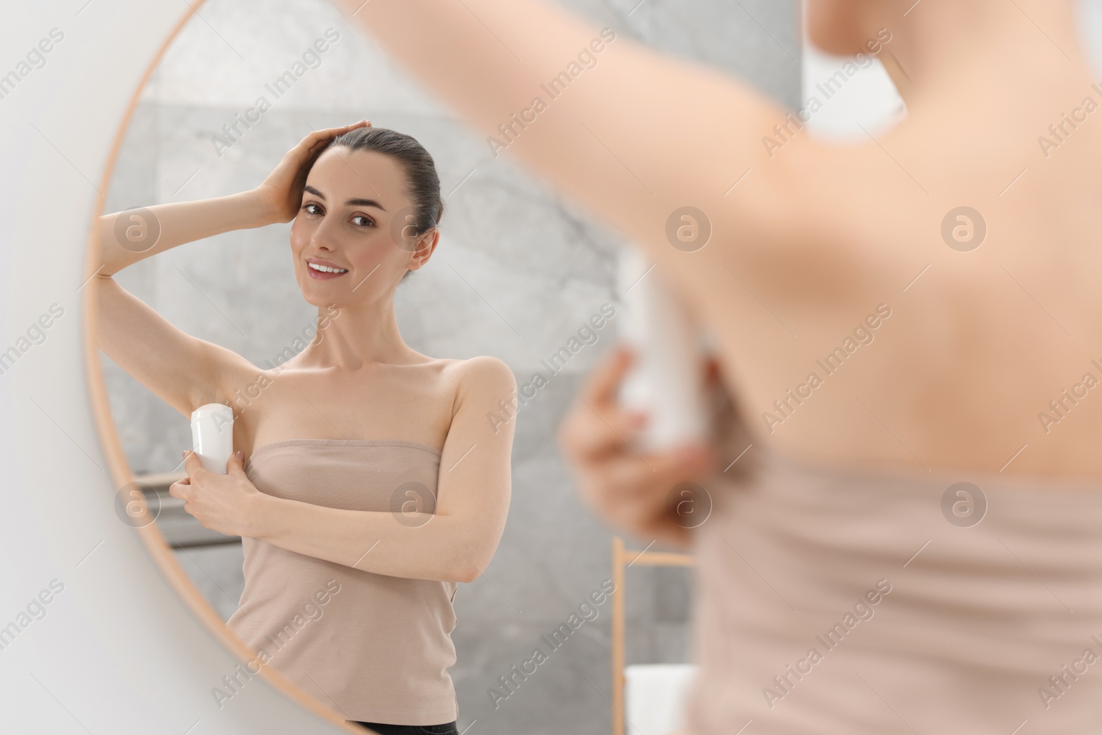 Photo of Beautiful woman applying deodorant near mirror in bathroom