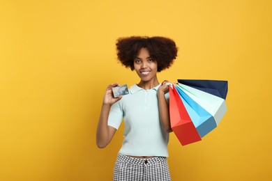 Photo of Happy African American woman with shopping bags and credit card on orange background. Space for text