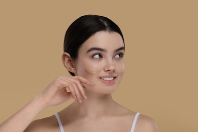 Photo of Teenage girl with swatch of foundation on face against beige background