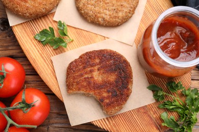 Delicious bitten vegan cutlets, ketchup, parsley and tomatoes on wooden table