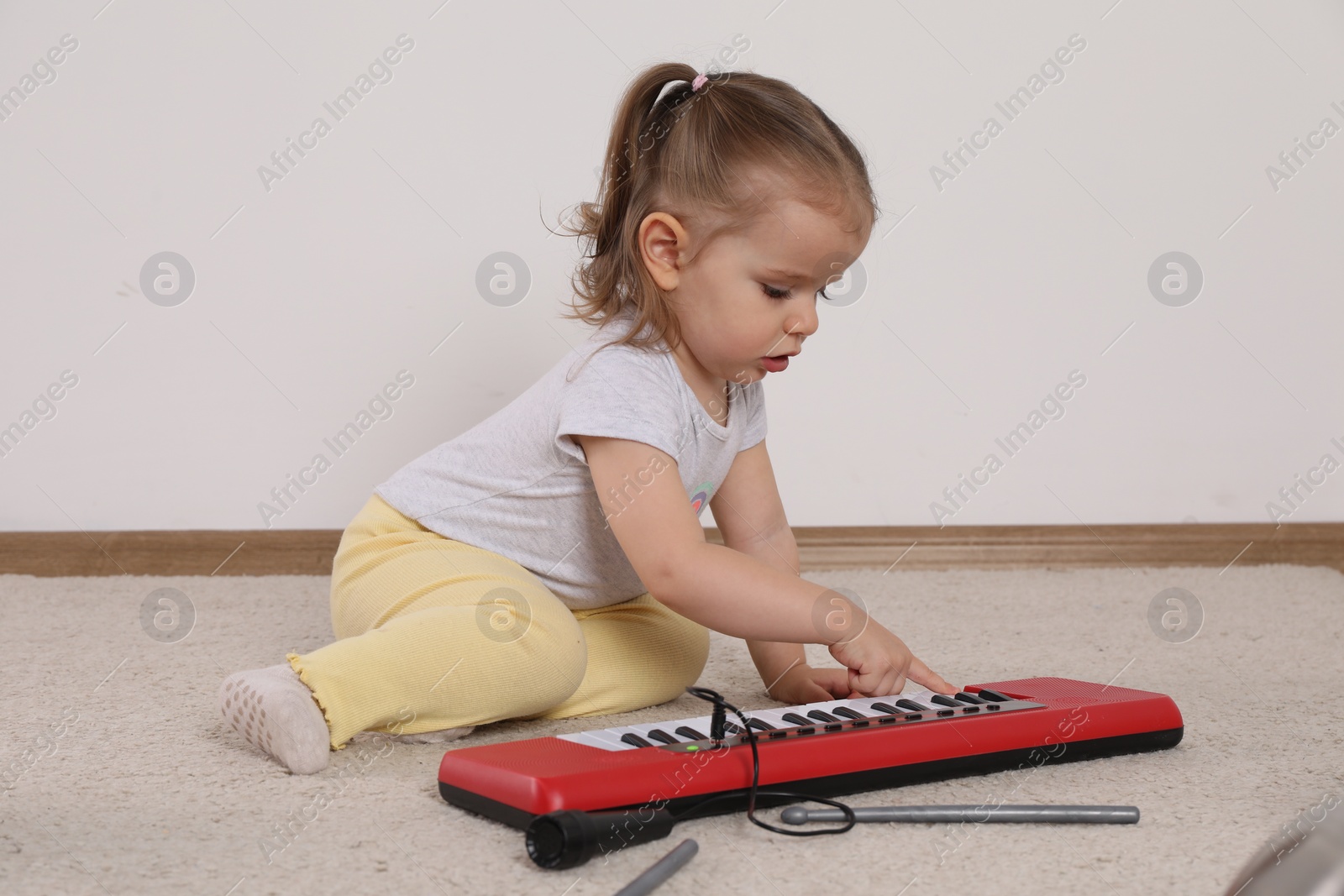 Photo of Cute little girl playing with toy piano at home