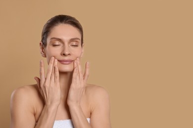 Woman massaging her face on beige background. Space for text
