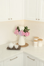 Photo of Beautiful bouquet of hydrangea flowers and tea on light countertop