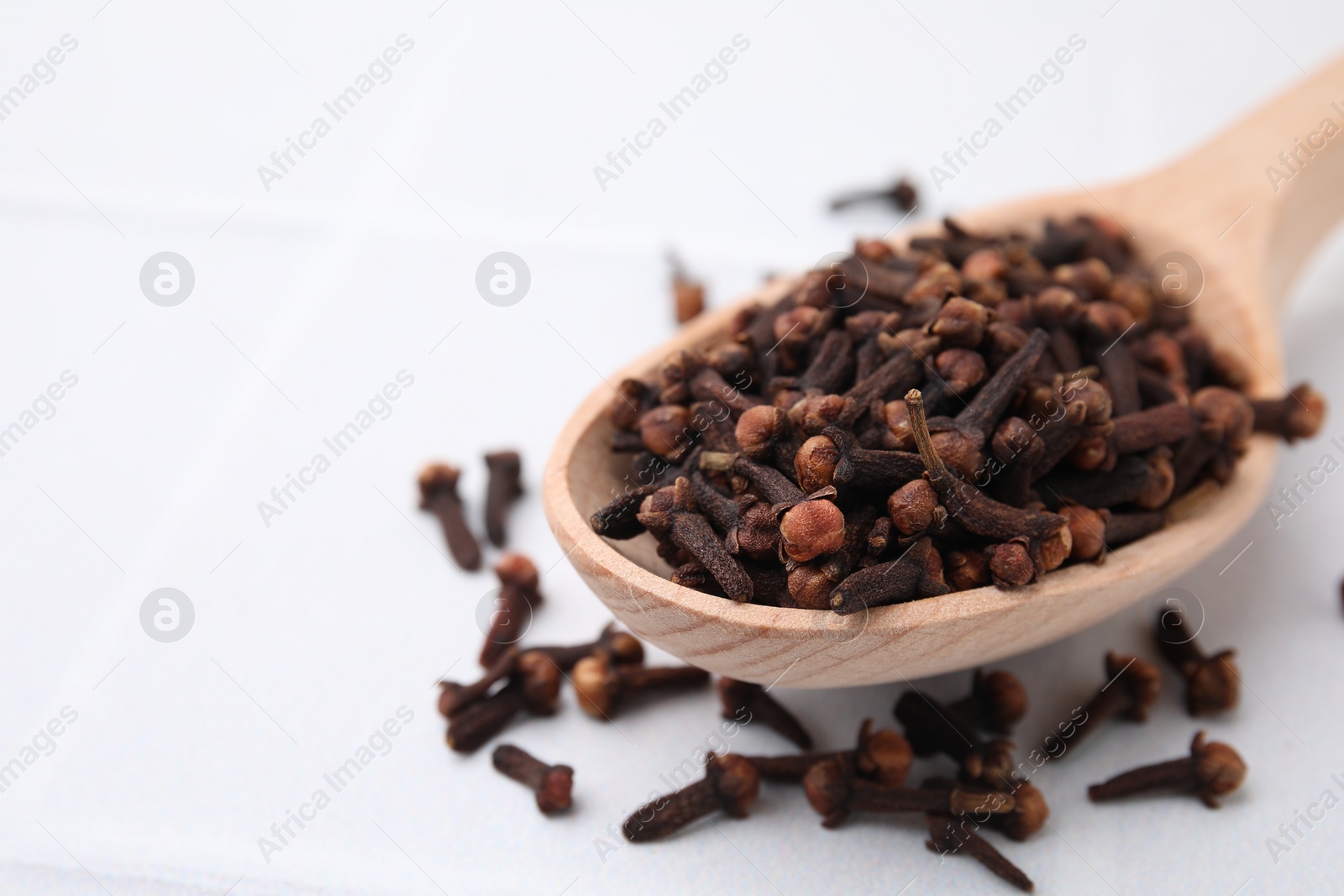 Photo of Spoon with aromatic dried clove buds on light table, closeup. Space for text