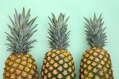 Photo of Whole ripe pineapples on light green background, flat lay