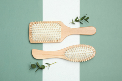 Photo of Wooden hair brushes and green twigs on color background, flat lay